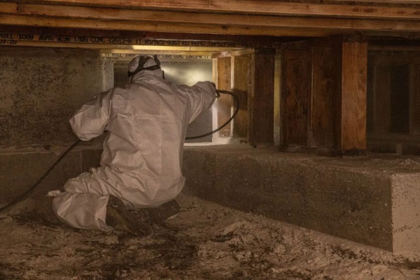 A man wearing a white suit sprays water on a concrete floor, part of a crawl space mold removal service in Las Vegas, NV.