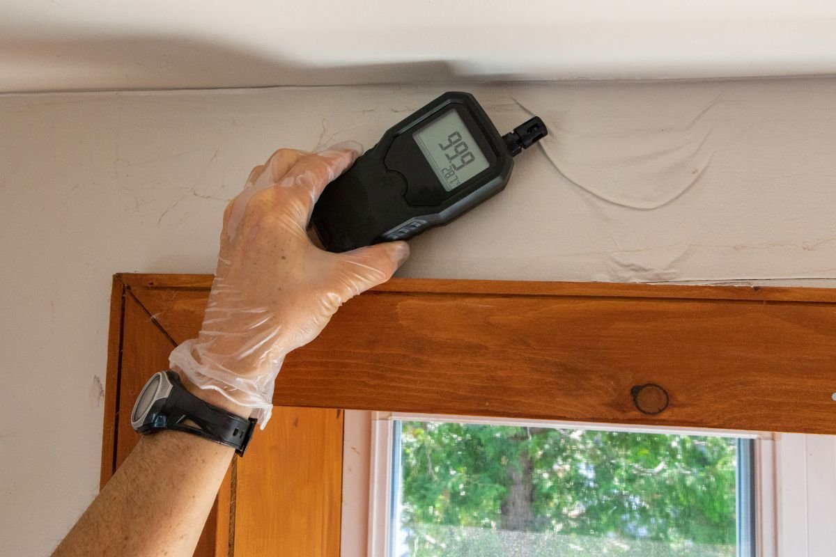 A person measuring the temperature of a window with a digital thermometer, highlighting the importance of air quality testing.