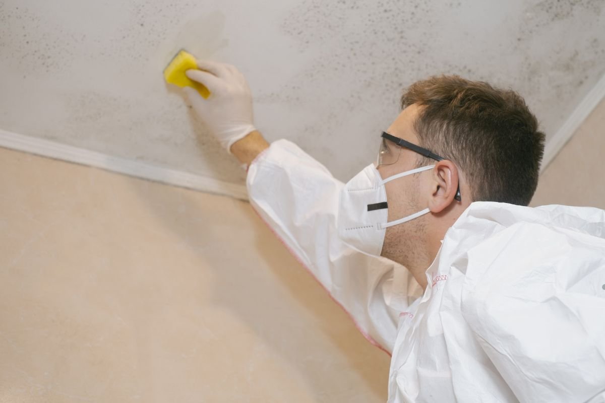 A man in a white coat and protective gear cleans a ceiling as part of a mold removal service.